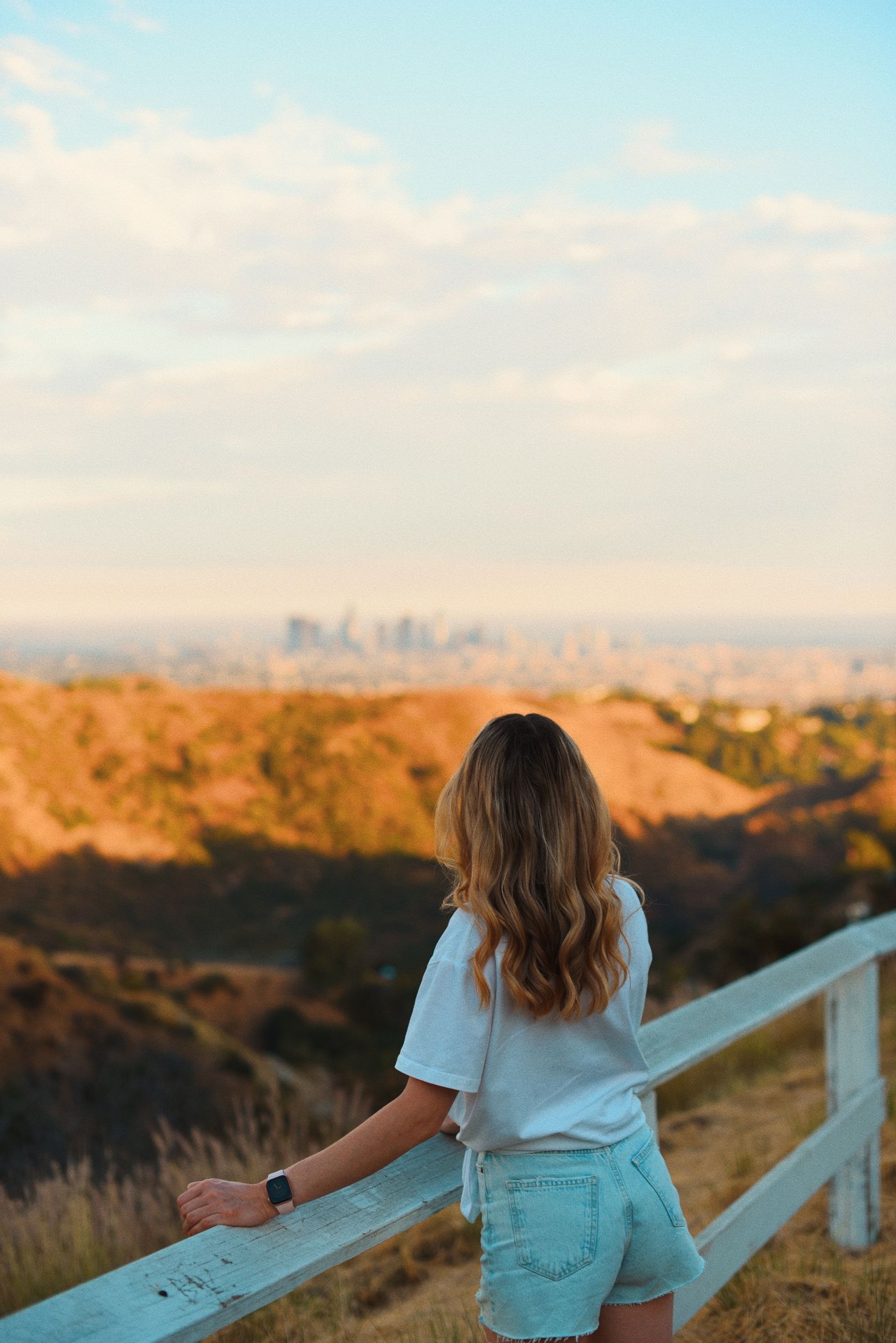 A young woman gazing at a city skyline from a scenic overlook at sunset